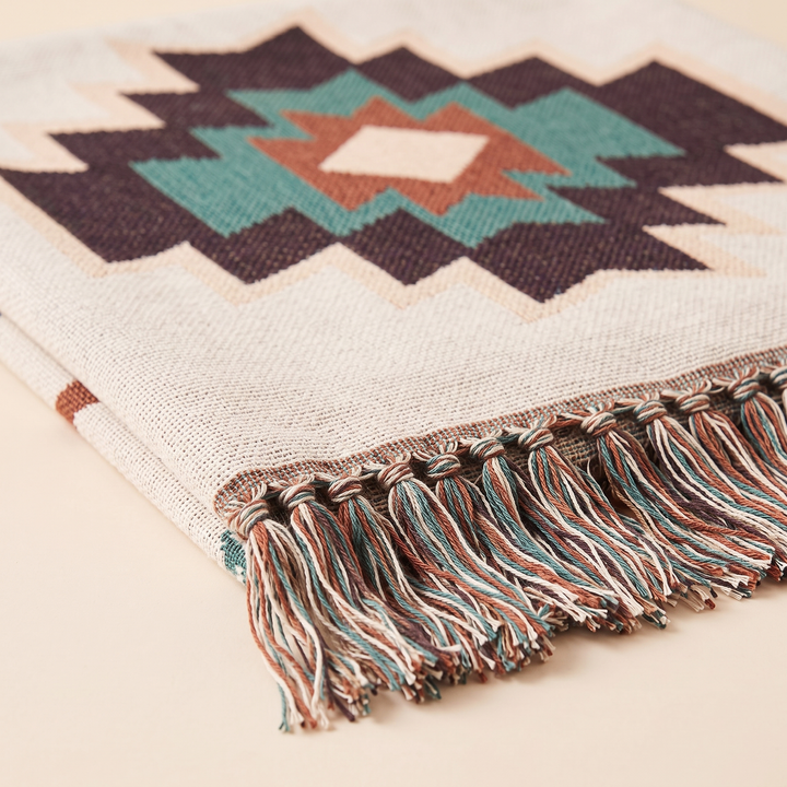 Aztec Throw Blanket – Woven in Cream Aztec – folded close-up of the fringed edge on a plain peach background