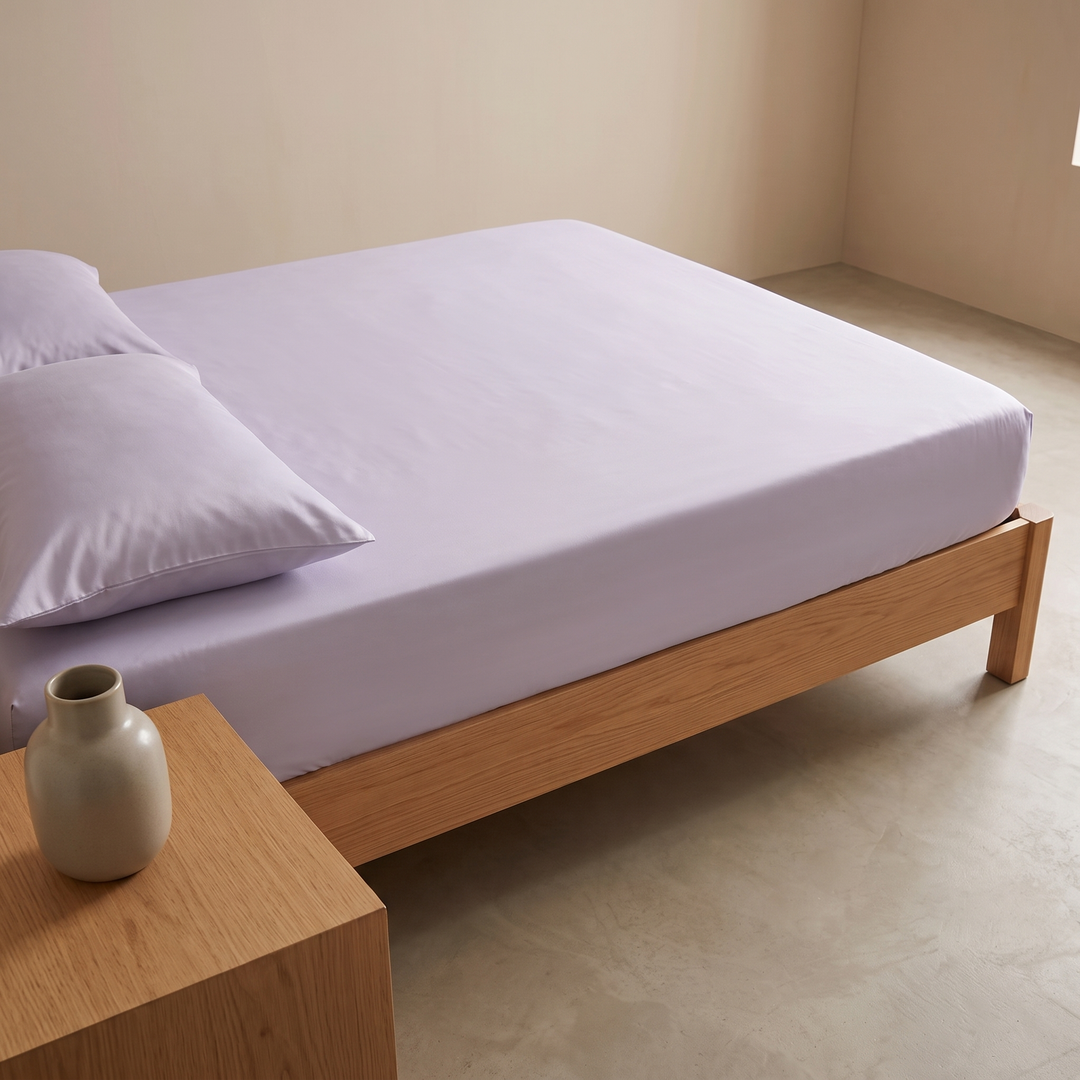 Bamboo Viscose Fitted Sheet Set with Pillowcases in Lavender – seen past a ceramic vase on an oak bedside table
