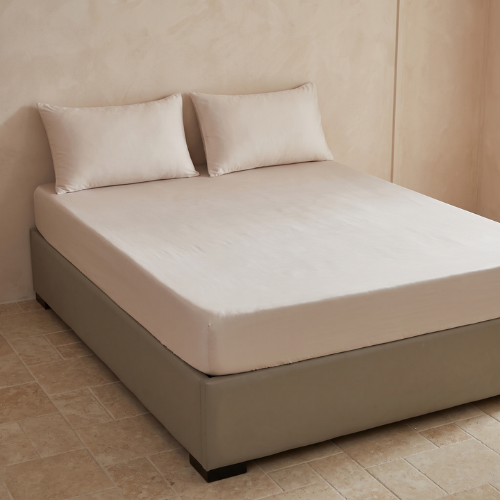 Bamboo Viscose Fitted Sheet Set with Pillowcases in Oatmeal – fitted on a upholstered bed with two pillowcases against a plaster wall