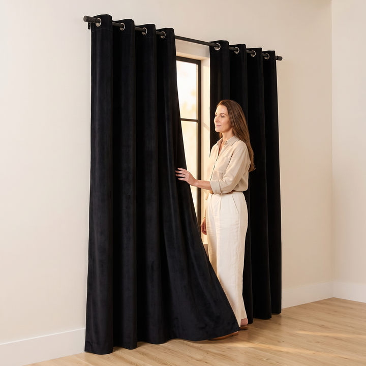 Black Velvet Curtain Panel – Grommet Top in Black – woman holding panel open beside window in bare room