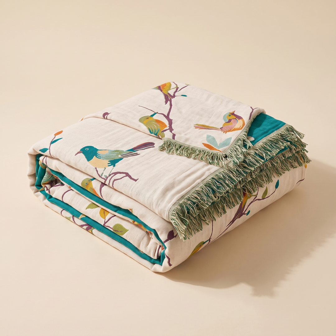 Boho Bird Bedspread – Reversible Gauze with Fringe in Cream – Songbirds – folded in a neat stack on a plain beige background