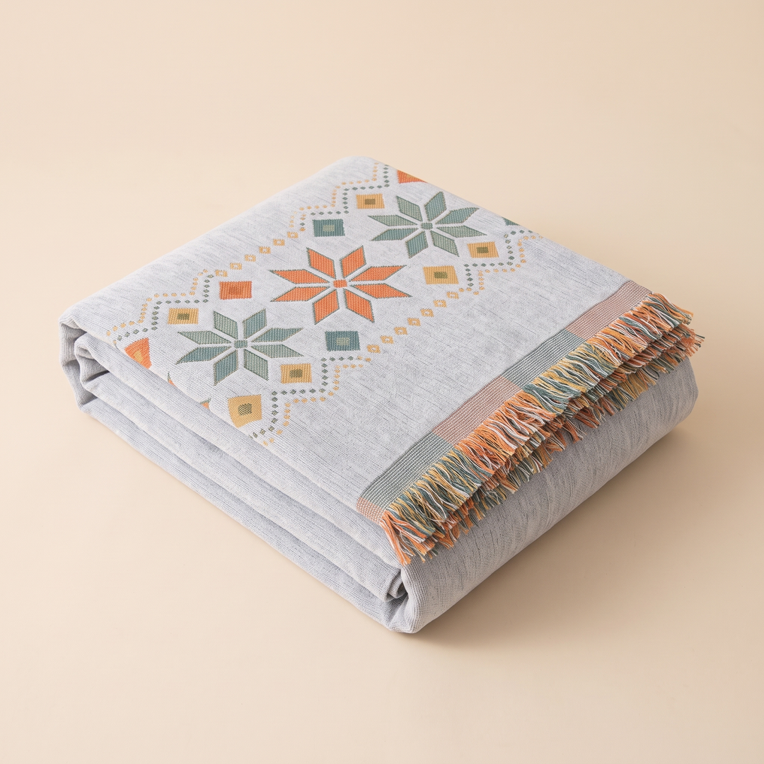 Boho Chenille Couch Cover with Fringe in Gray – folded neatly on a plain peach background, fringe visible
