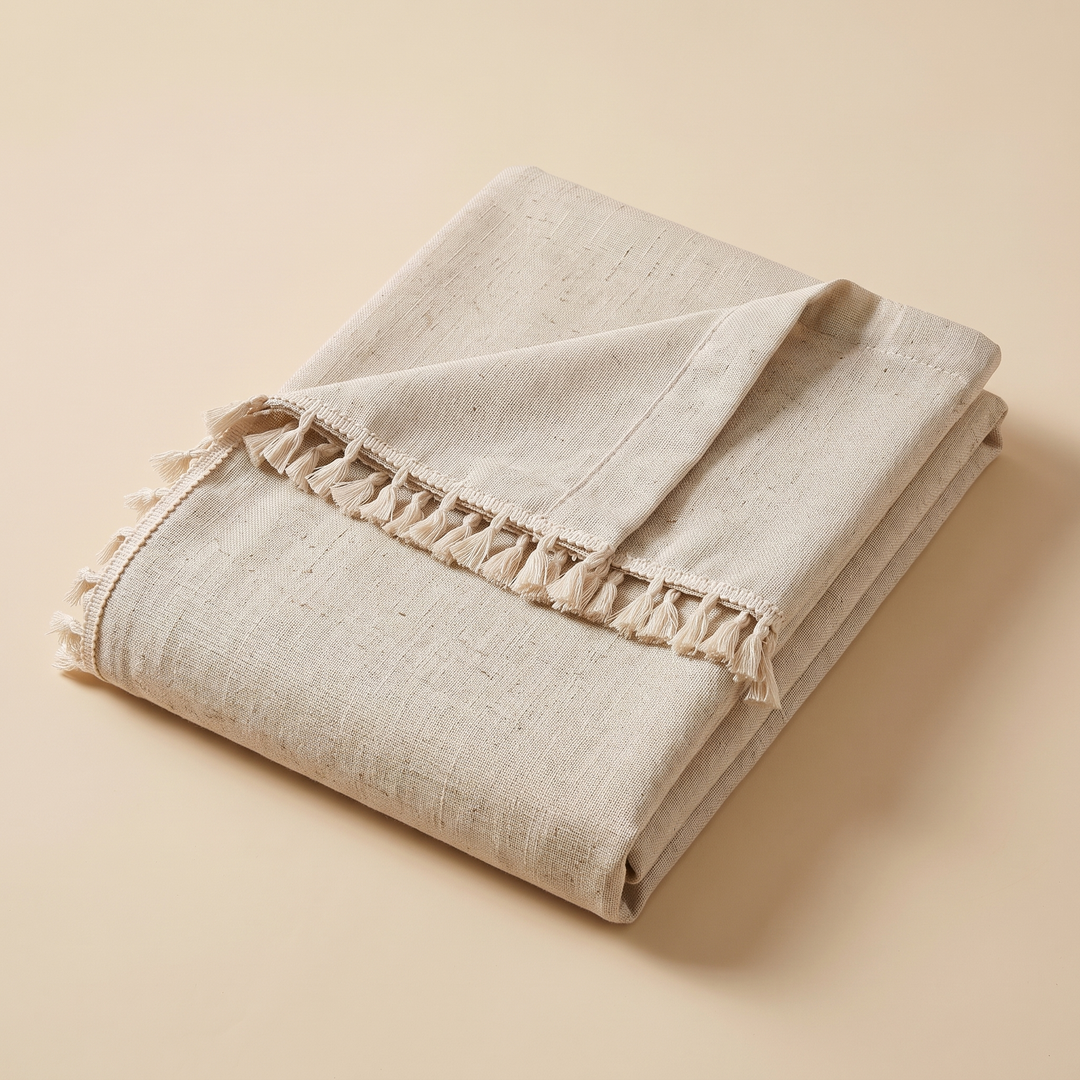 Boho Curtain Panel – Linen Look, Rod Pocket in Oatmeal – Tassel – folded neatly on a plain peach background with tassels visible