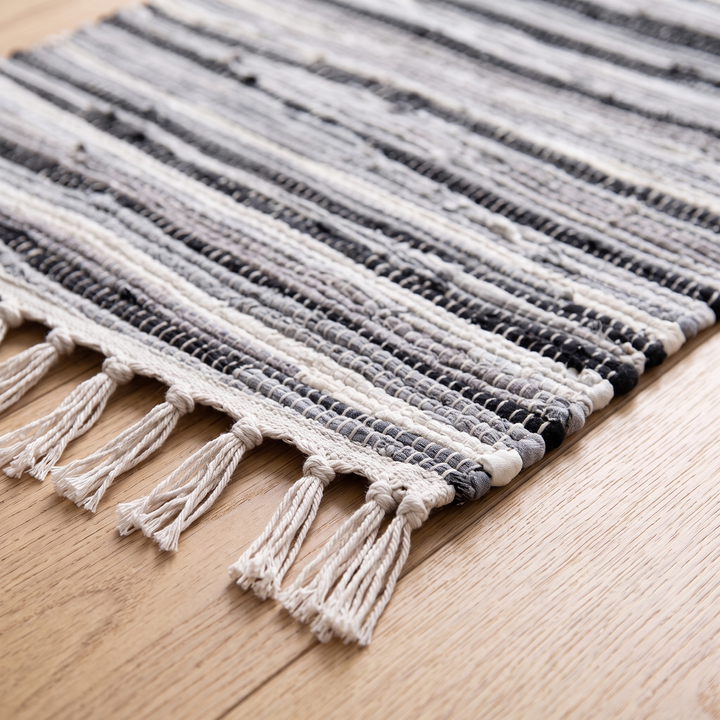 Boho Rag Rug – Woven Cotton Stripes in Gray – close-up of fringed corner on a light wood floor