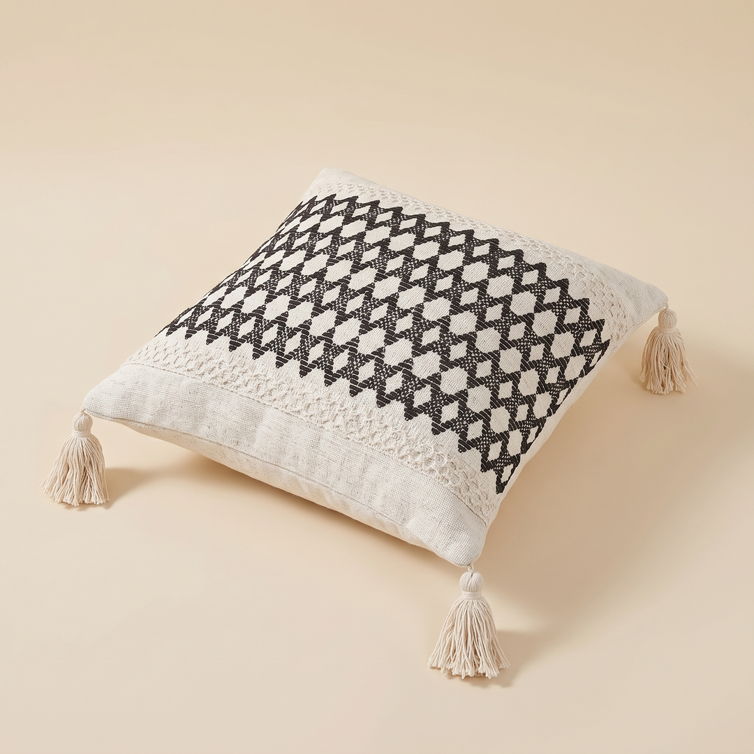 Boho Pillow Cover with Tassels – Woven in Cream – Black Diamond – plumped and filled, lying flat on a warm sandy surface