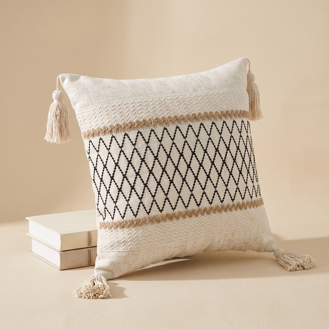 Boho Pillow Cover with Tassels – Woven in Cream – Black Lattice – leaning against a stack of two hardcover books
