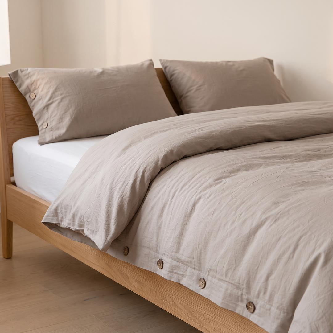 Cotton Duvet Cover Set with Buttons in Taupe – three-quarter view of button-edged pillowcases and rumpled duvet corner