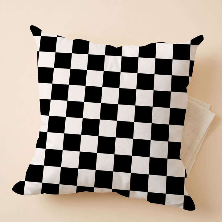 Checkered Pillow Cover in Black &amp; White Check – tilted on a folded beige cloth over a peach backdrop