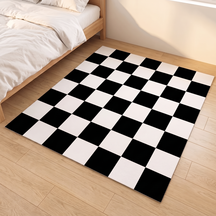Washable Checkered Rug – Black and White in Black and White – laid flat on a wood floor beside a bed