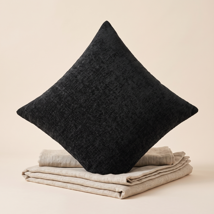 Chenille Throw Pillow Cover in Black – standing on its corner atop folded beige linens