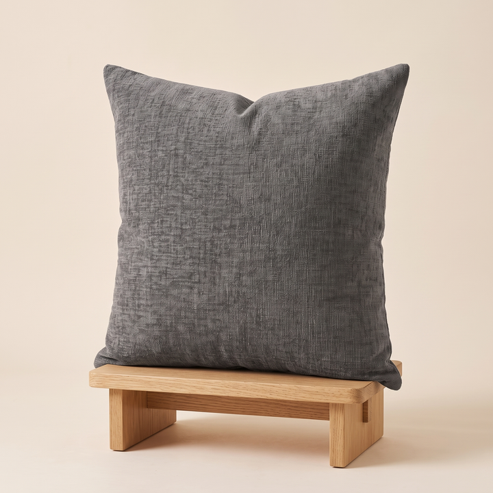 Chenille Throw Pillow Cover in Charcoal – propped upright on a low oak wood stool