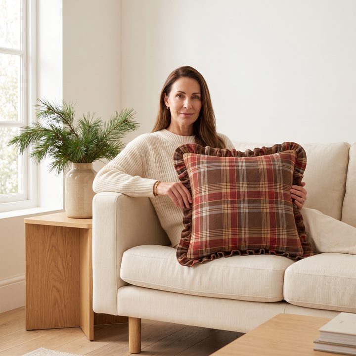Christmas Plaid Pillow Cover in Brown – Tartan – held by a seated woman on a cream sofa in a living room