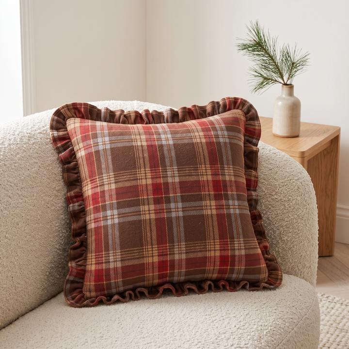 Christmas Plaid Pillow Cover in Brown – Tartan – propped on a cream boucle armchair beside a wooden side table