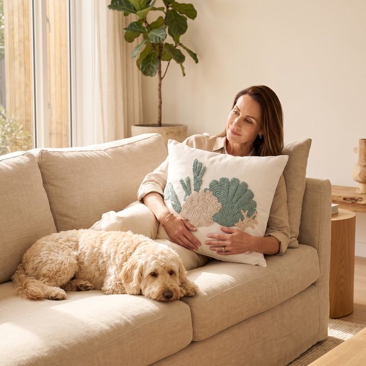 Coastal Throw Pillow Cover – Tufted in Sea Green – Shell – held by a seated woman on a sofa beside a sleeping dog