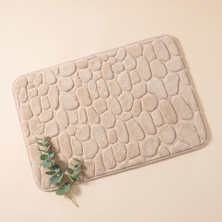 Non-Slip Memory Foam Bath Mat – Cobblestone in Beige – top-down view with a eucalyptus sprig resting on one corner