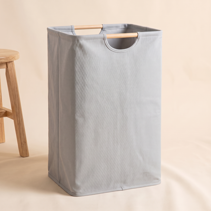 Collapsible Laundry Basket in Pale Gray – standing beside a small wooden stool, side angle