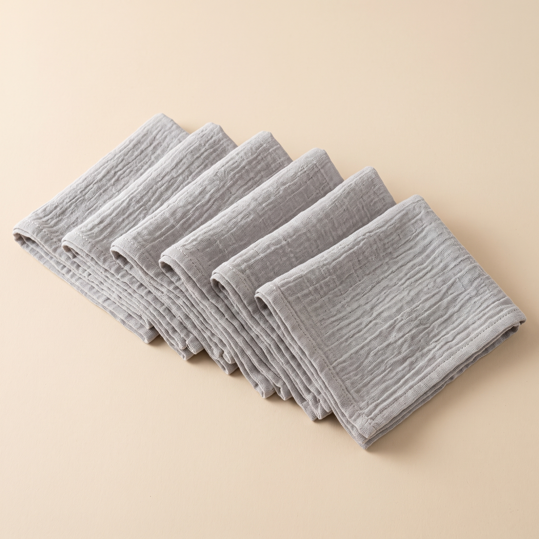 Cotton Gauze Napkins – Set of 6 in Gray – six folded napkins fanned out in an overlapping row on a beige background