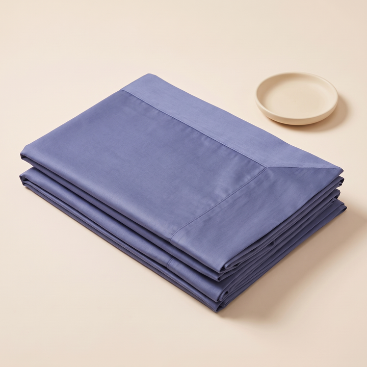 Cotton Sateen Pillowcases – Set of 2 in Blue – three-quarter view of folded stack beside a small ceramic dish