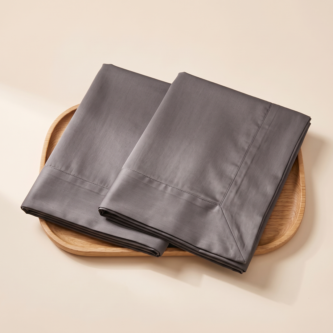 Cotton Sateen Pillowcases – Set of 2 in Charcoal – folded and overlapping on a rounded smooth wooden tray