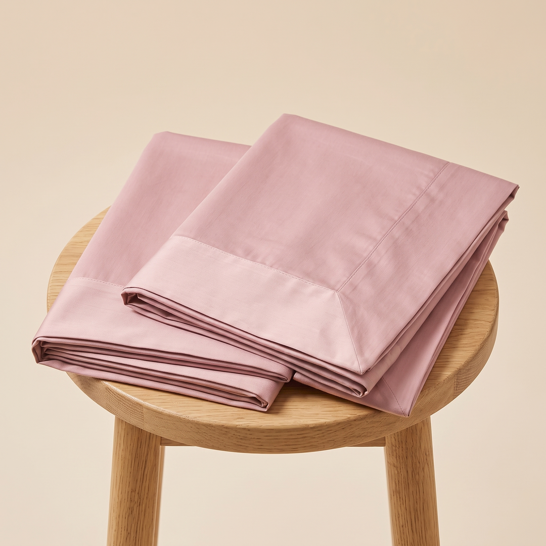 Cotton Sateen Pillowcases – Set of 2 in Dusty Pink – two folded pillowcases resting on a round wooden stool