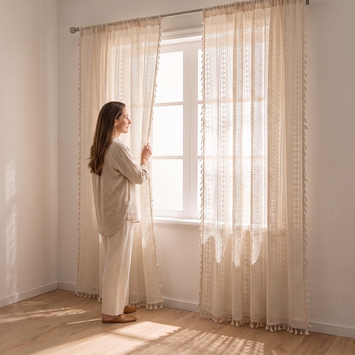 Crochet Lace Curtain Panel – Boho Tassel Trim in Cream – woman drawing back a panel at a bright window