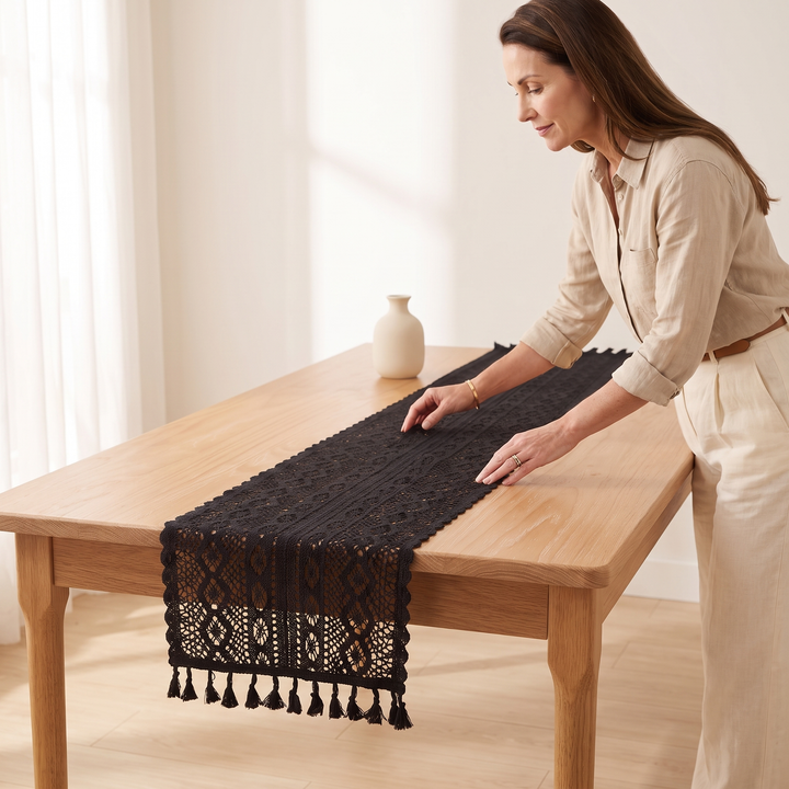 Crochet Table Runner in Black – Tasseled Ends – being smoothed flat along an oak table by a woman
