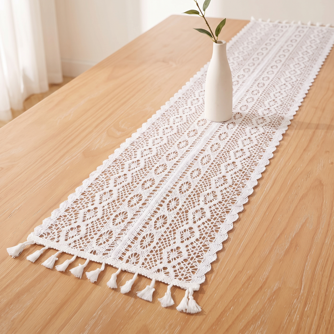 Crochet Table Runner in White – Tasseled Ends – diagonal view with leafy sprig in vase, sheer curtain behind