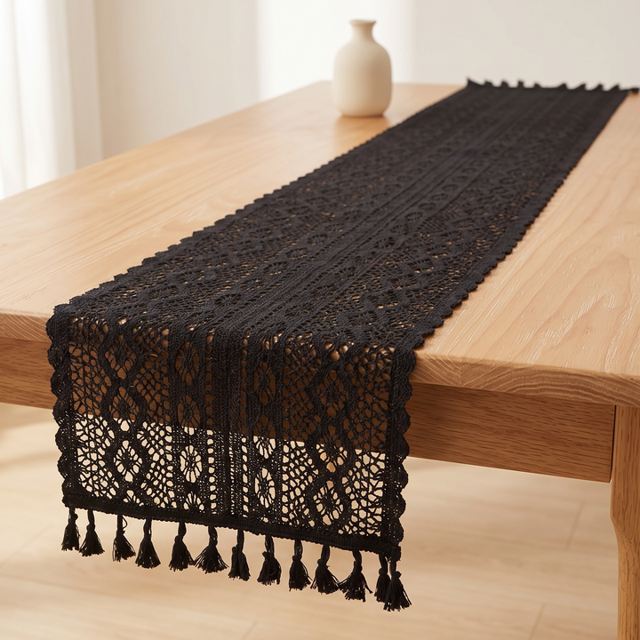 Crochet Table Runner in Black – Tasseled Ends – draped lengthwise over a wooden table with a vase