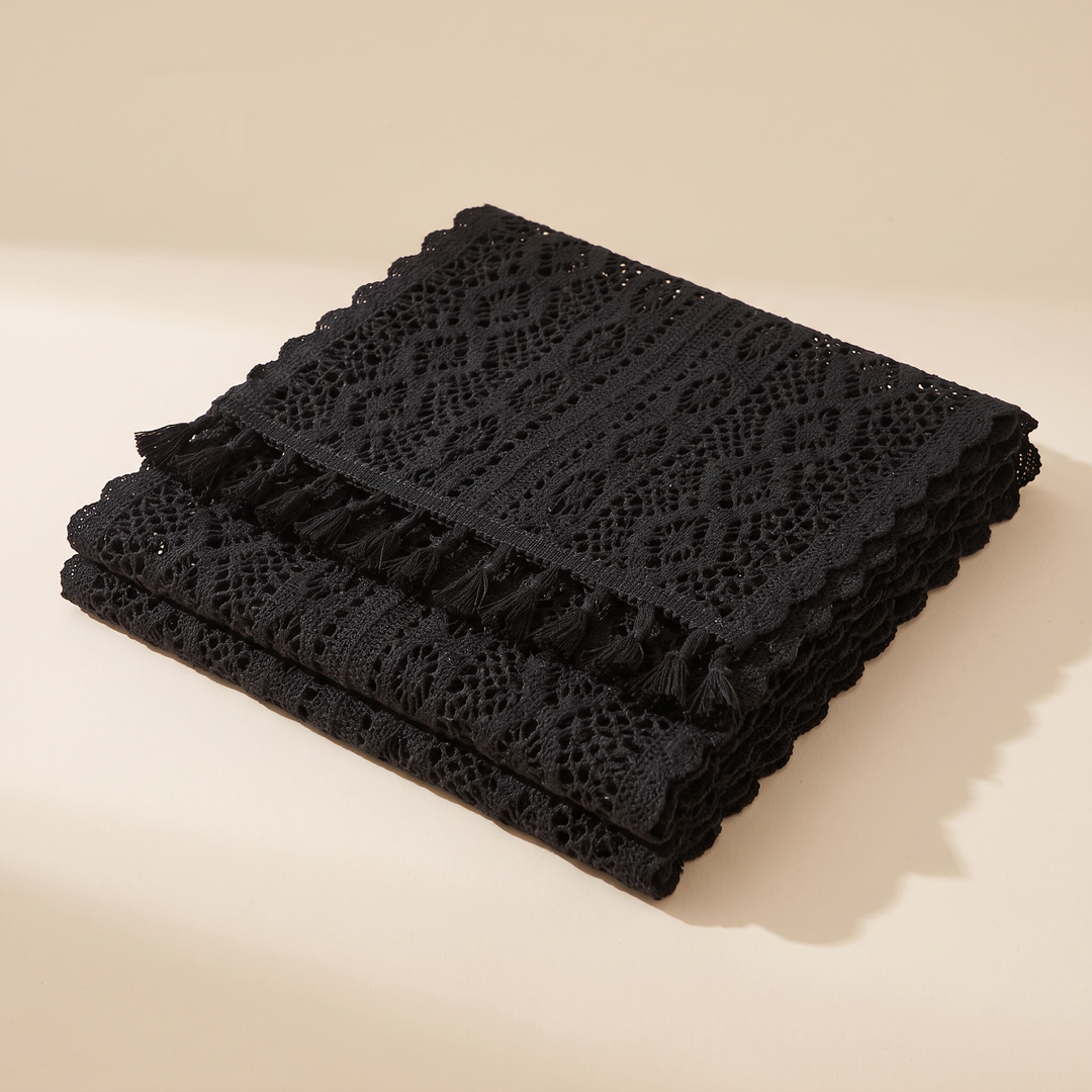Crochet Table Runner in Black – Tasseled Ends – folded in a neat stack on a plain cream surface