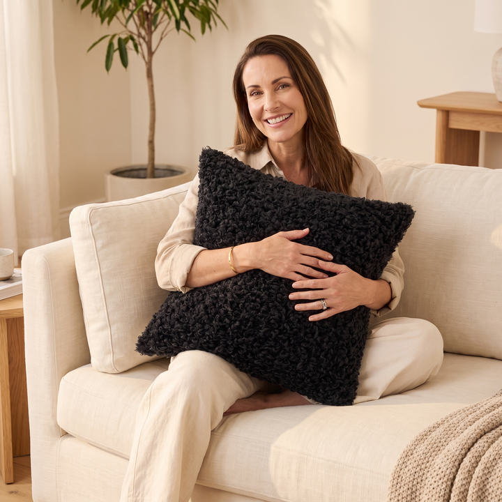 Curly Faux Fur Pillow Cover in Black – held by a smiling woman seated on a sofa