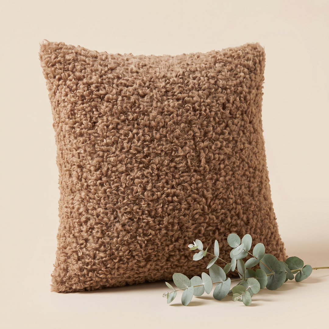 Curly Faux Fur Pillow Cover in Chocolate Brown – standing upright beside a sprig of eucalyptus on cream
