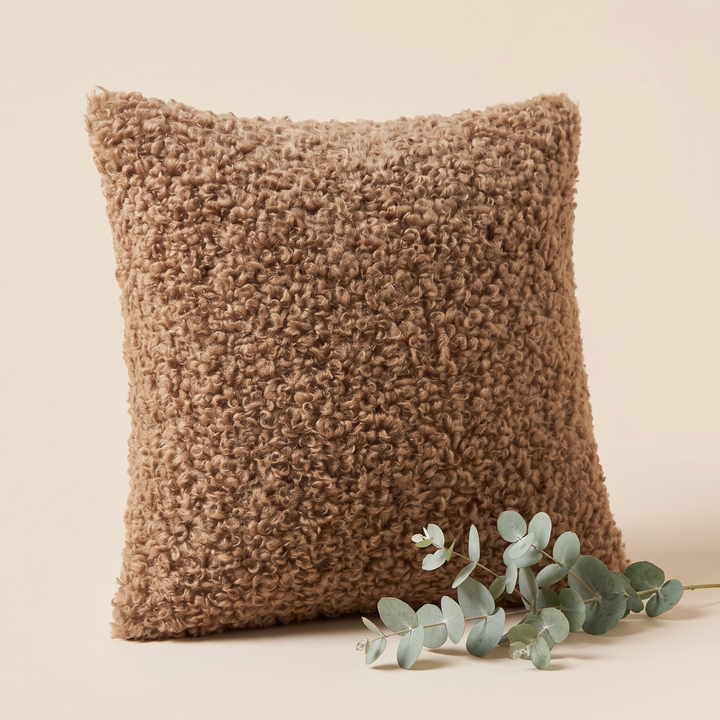 Curly Faux Fur Pillow Cover in Chocolate Brown – standing upright beside a sprig of eucalyptus on cream
