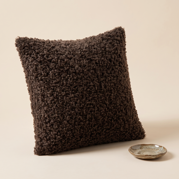 Curly Faux Fur Pillow Cover in Dark Brown – angled three-quarter view beside a small speckled ceramic dish
