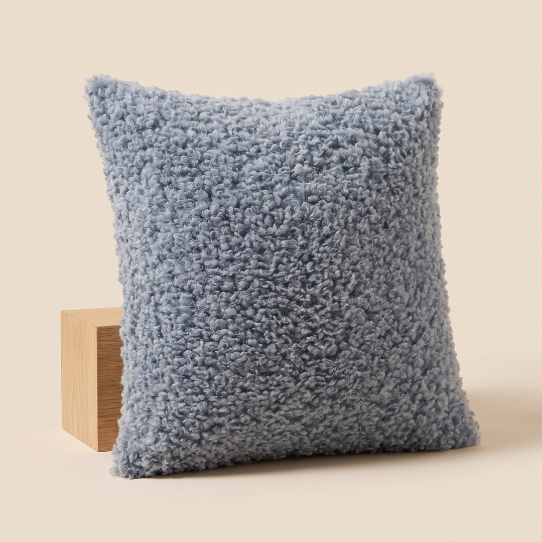 Curly Faux Fur Pillow Cover in Dusty Blue – tilted against a pale wood cube with soft shadow