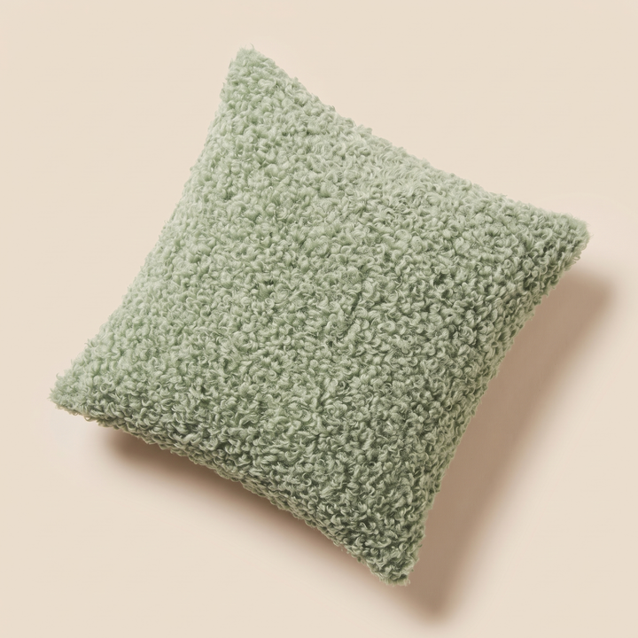 Curly Faux Fur Pillow Cover in Sage – angled overhead view on pale peach surface