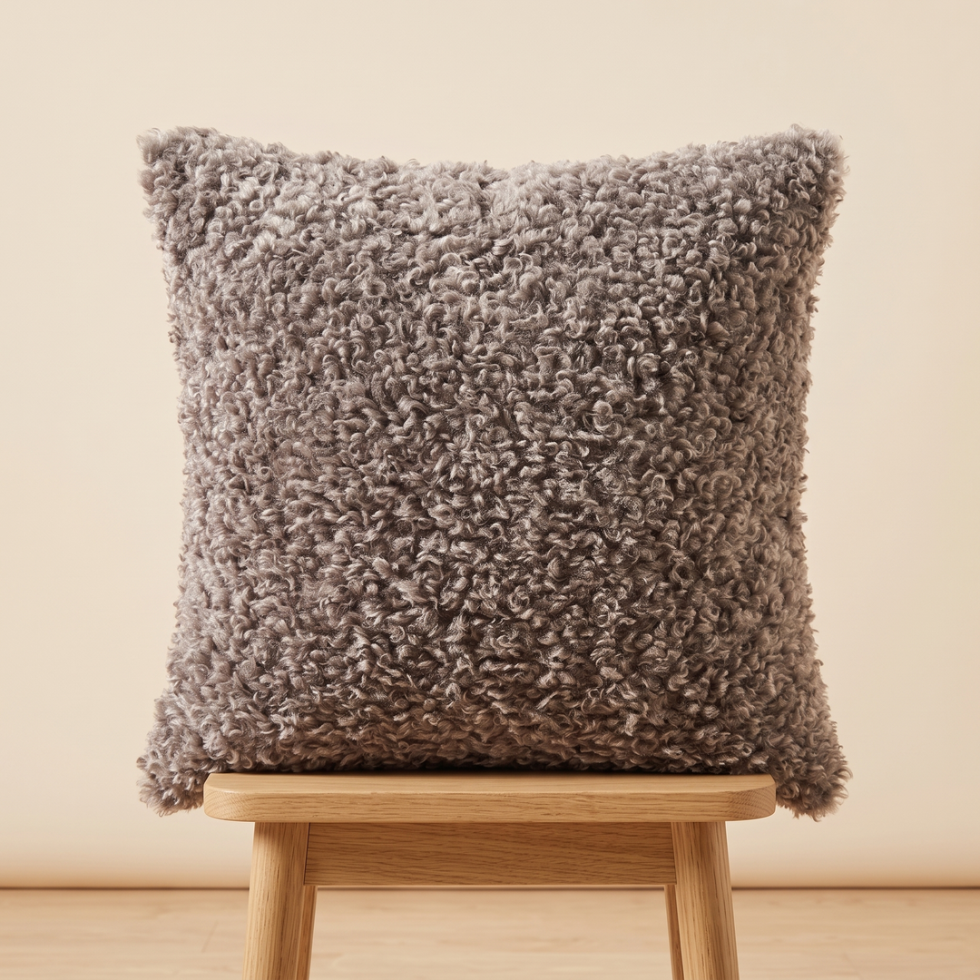 Curly Faux Fur Pillow Cover in Taupe – upright on a light wood stool against a cream wall