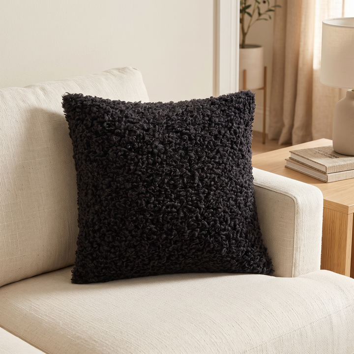 Curly Faux Fur Pillow Cover in Black – propped in the corner of a cream sofa beside a side table