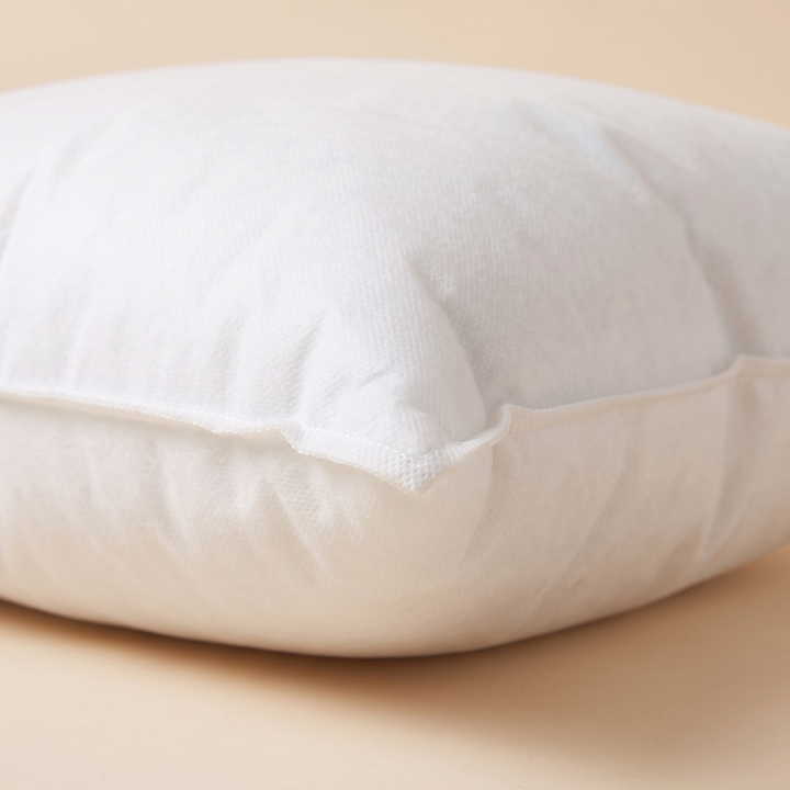 Throw Pillow Insert in White – close-up of the corner seam and nonwoven fabric on a peach surface