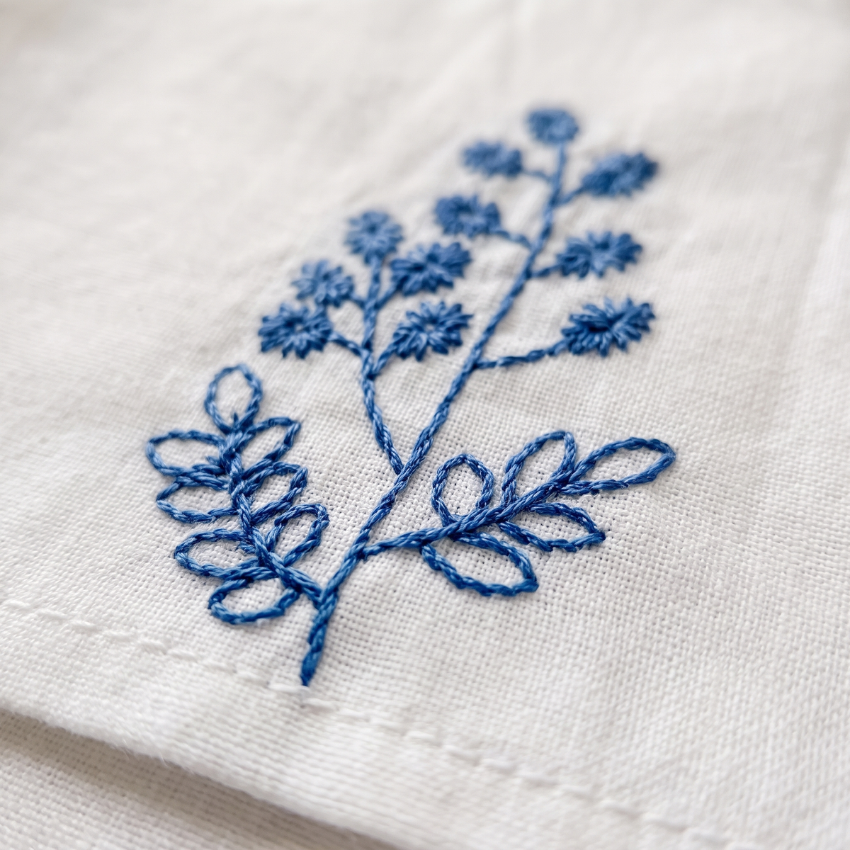 Embroidered Cotton Napkins – Set of 6 in White – Botanical – close-up of blue embroidered sprig on a hemmed corner