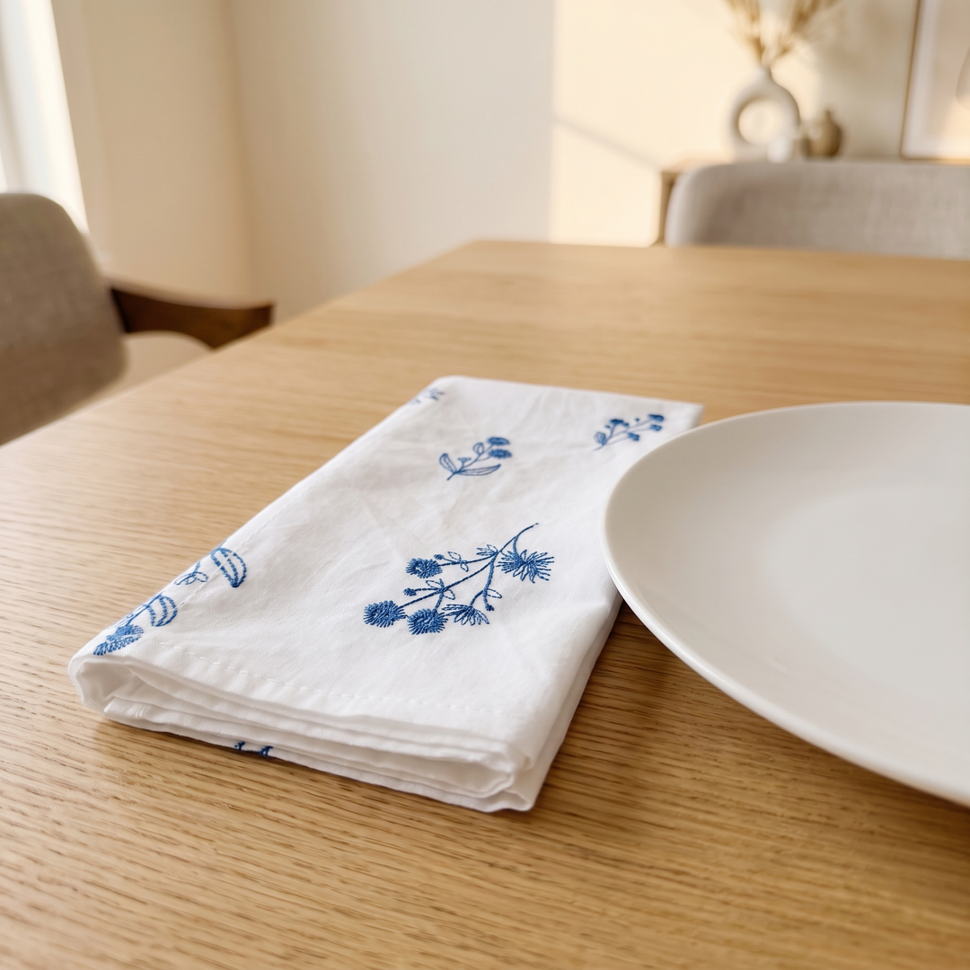 Embroidered Cotton Napkins – Set of 6 in White – Botanical – folded on a light wood dining table beside a white plate
