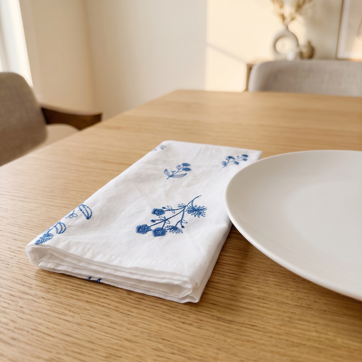 Embroidered Cotton Napkins – Set of 6 in White – Botanical – folded on a light wood dining table beside a white plate