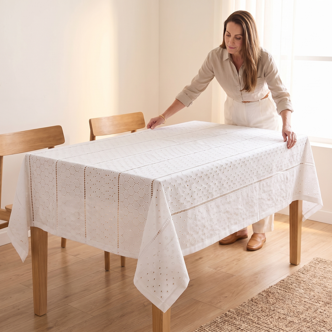 White Cotton Tablecloth – Embroidered in White – Eyelet Circles – being smoothed over a dining table by a woman in a sunlit room