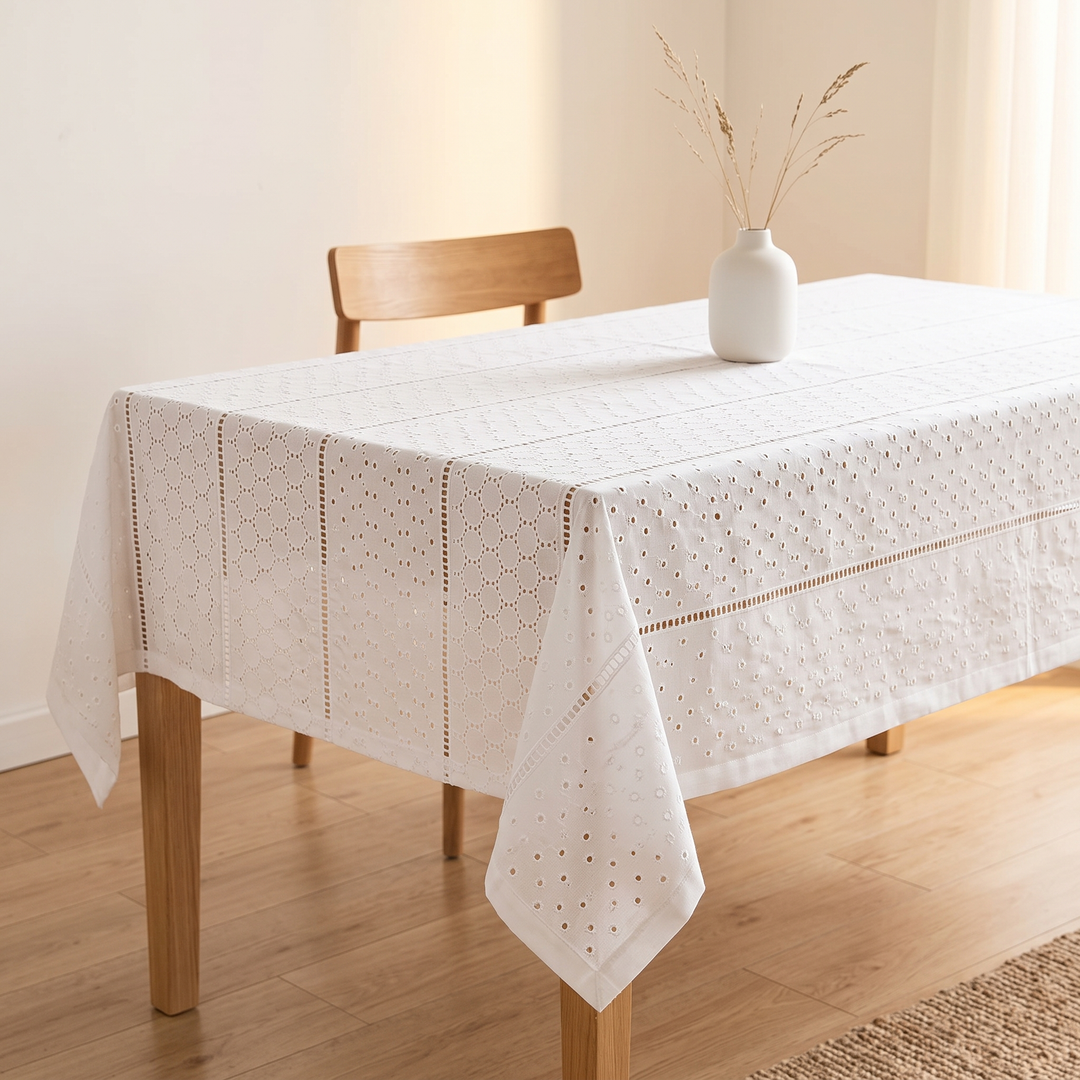 White Cotton Tablecloth – Embroidered in White – Eyelet Circles – draped over a wooden dining table with vase and chair