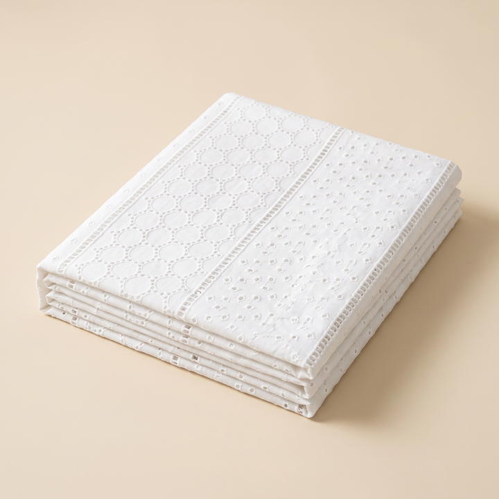 White Cotton Tablecloth – Embroidered in White – Eyelet Circles – folded neatly in a stack on a plain beige background