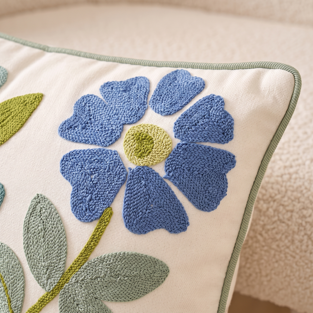 Embroidered Botanical Pillow Cover in Cream – Blue Floral – close-up of the embroidered flower and piped edge on a boucle seat