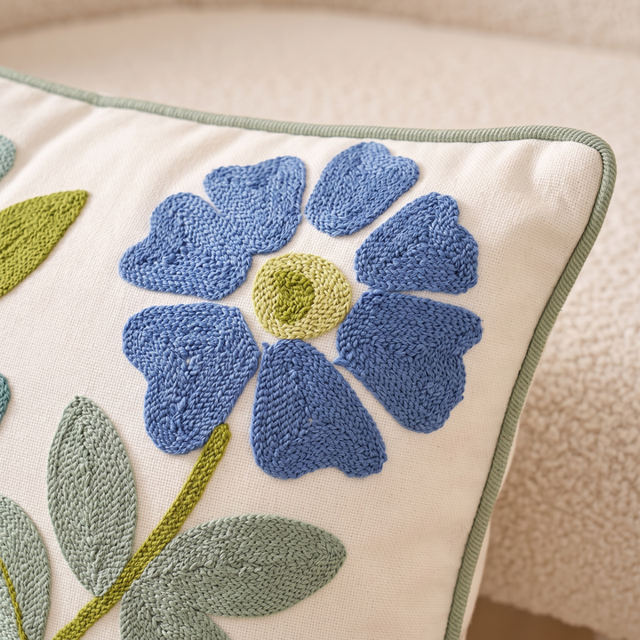 Embroidered Botanical Pillow Cover in Cream – Blue Floral – close-up of the embroidered flower and piped edge on a boucle seat