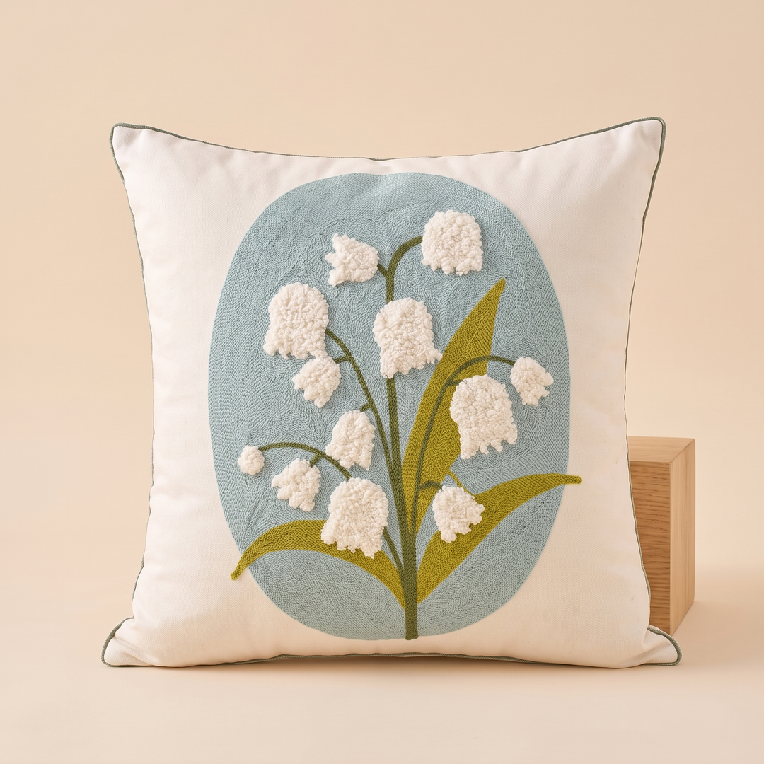 Embroidered Botanical Pillow Cover in Cream – Aqua Lily of the Valley – leaning against a light wooden block, shown straight on