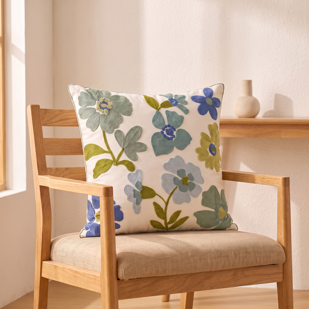 Embroidered Botanical Pillow Cover in Cream – Blue Floral – propped on a wooden chair beside a sunlit window