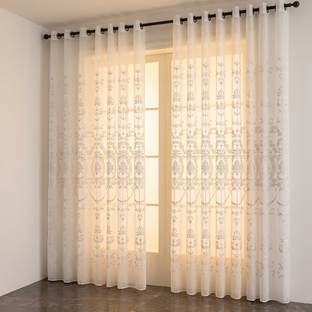 Embroidered Sheer Curtain Panel – Grommet Top in White – two panels hanging on a black rod beside a glowing window