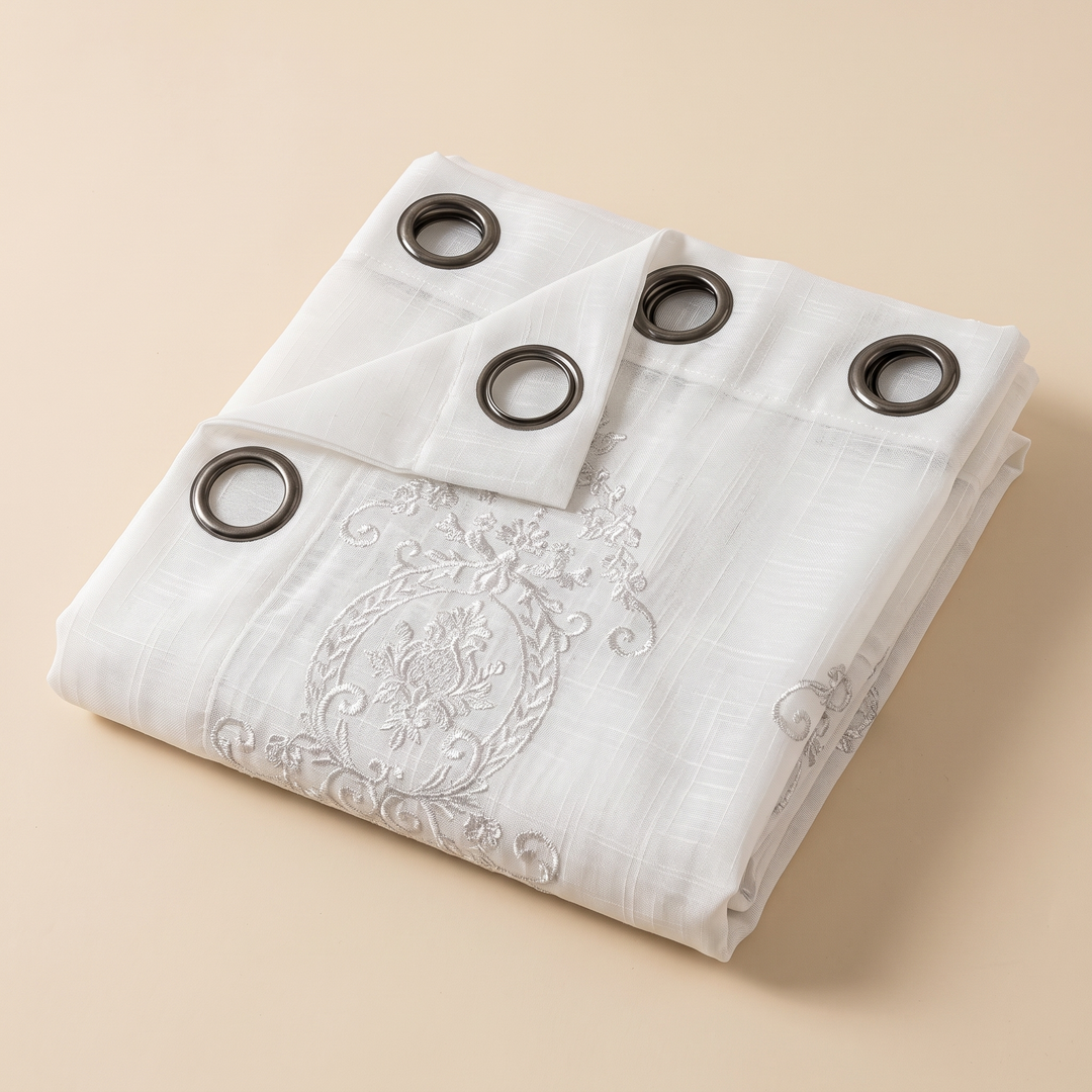 Embroidered Sheer Curtain Panel – Grommet Top in White – folded neatly on a beige surface showing grommets and embroidery